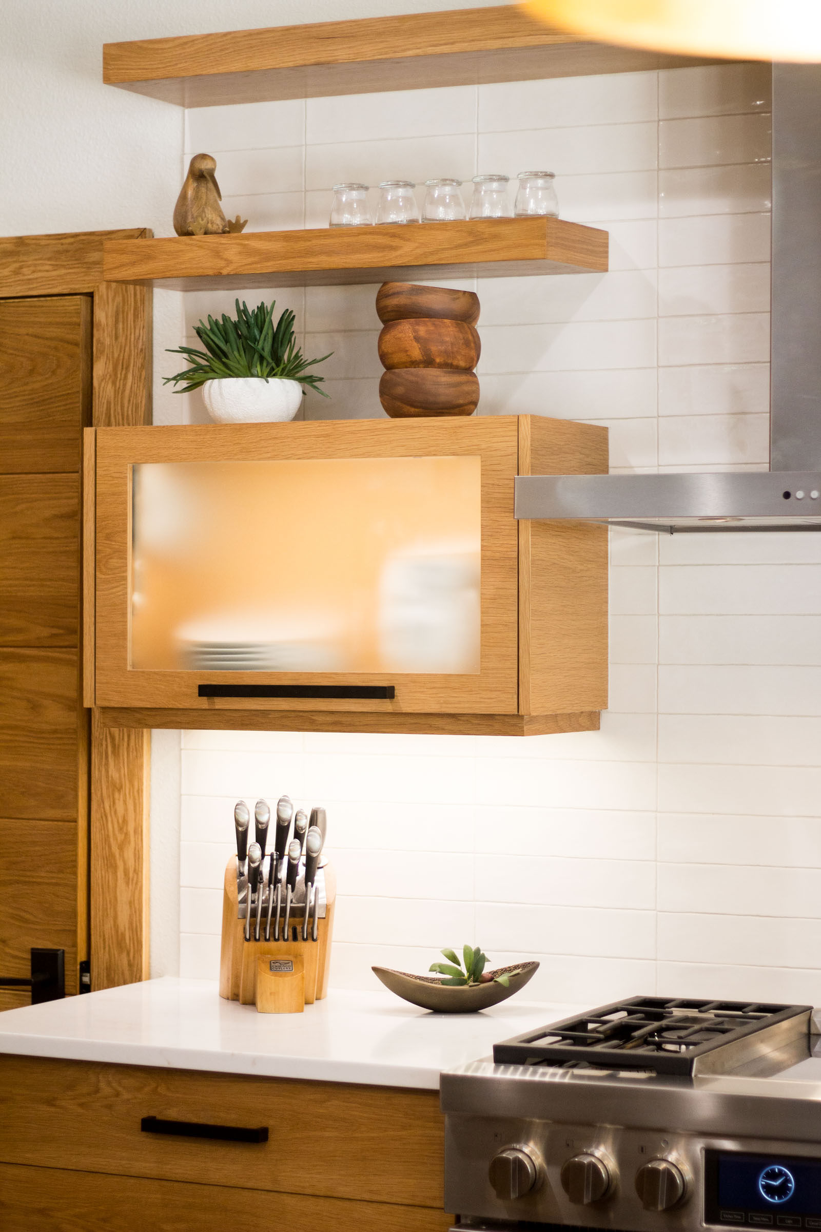 Stainless steel gas cooktop, exposed shelves, succulents, vertical lift cabinets made of blonde wood