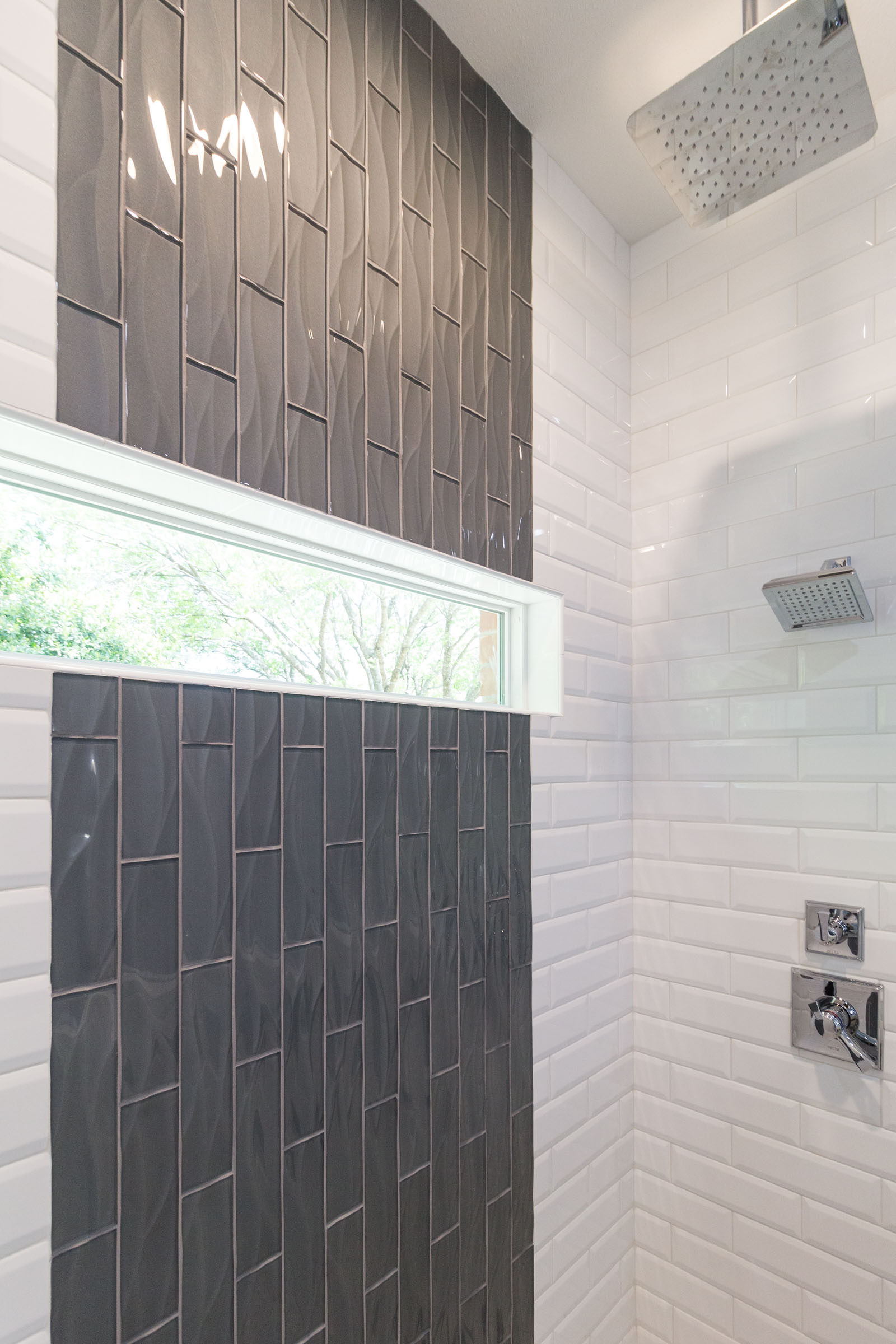 Contemporary bathroom remodel with vertical grey glass tile, white subway tile, and chrome shower heads