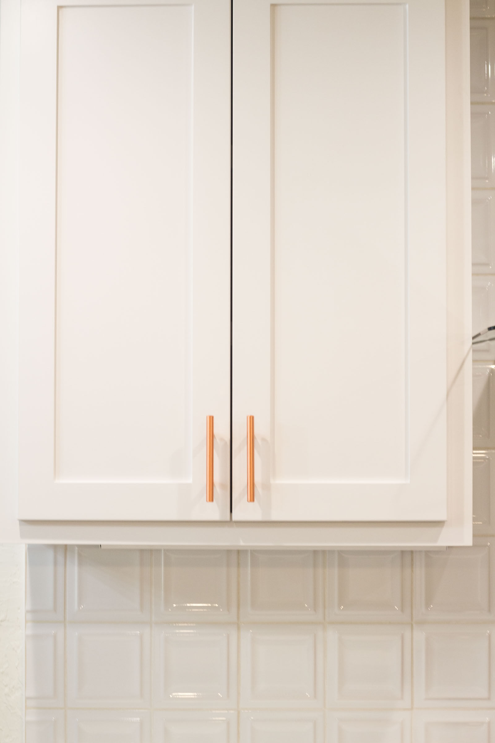 White shaker cabinets and backsplash with copper hardware