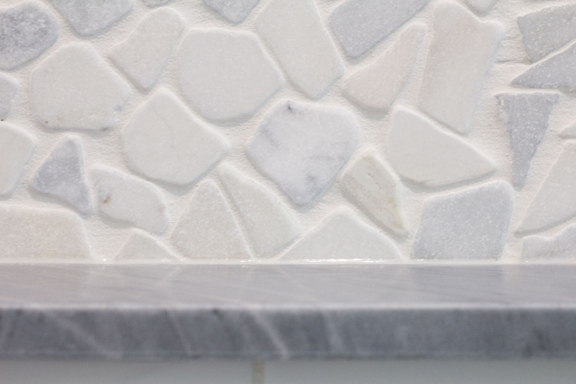 Close up shot of bathroom remodel with grey granite and multicolor pebble backsplash tile