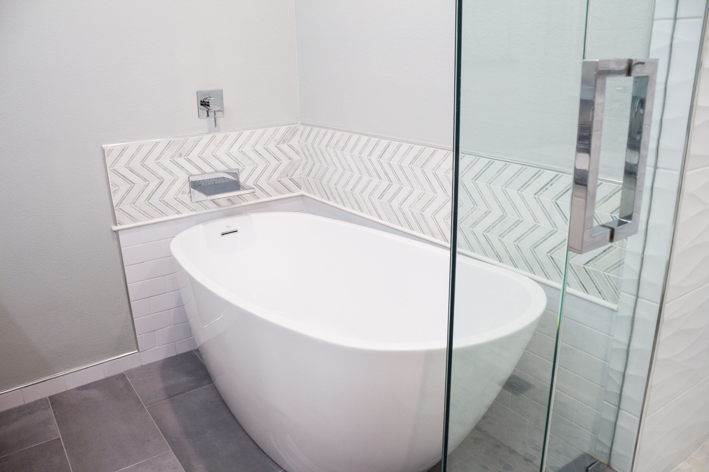 Bathroom remodel with white pedestal tub, chevron backsplash, grey tile, and chrome waterfall faucet