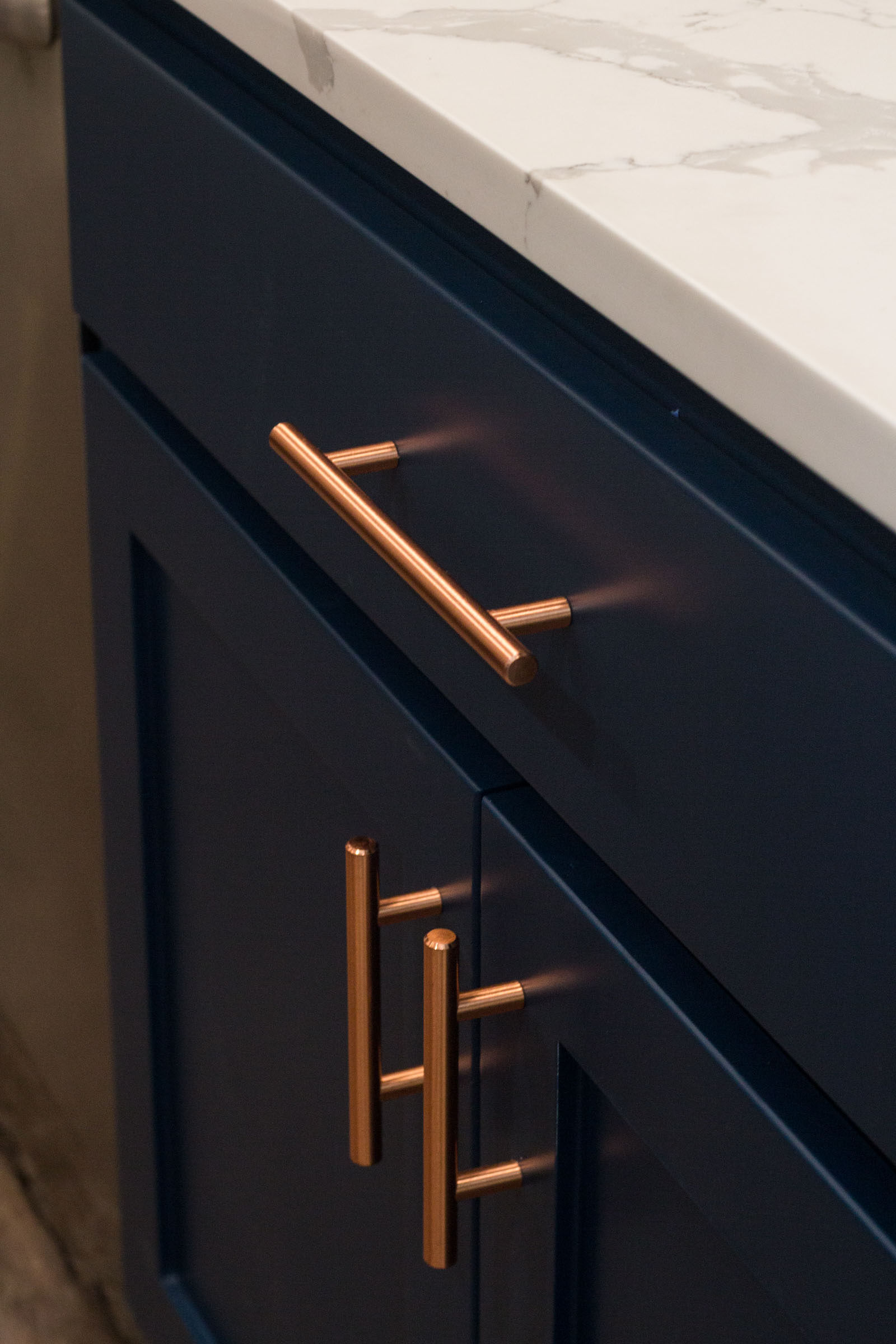 Close up of navy cabinets and copper hardware with white marble style counters