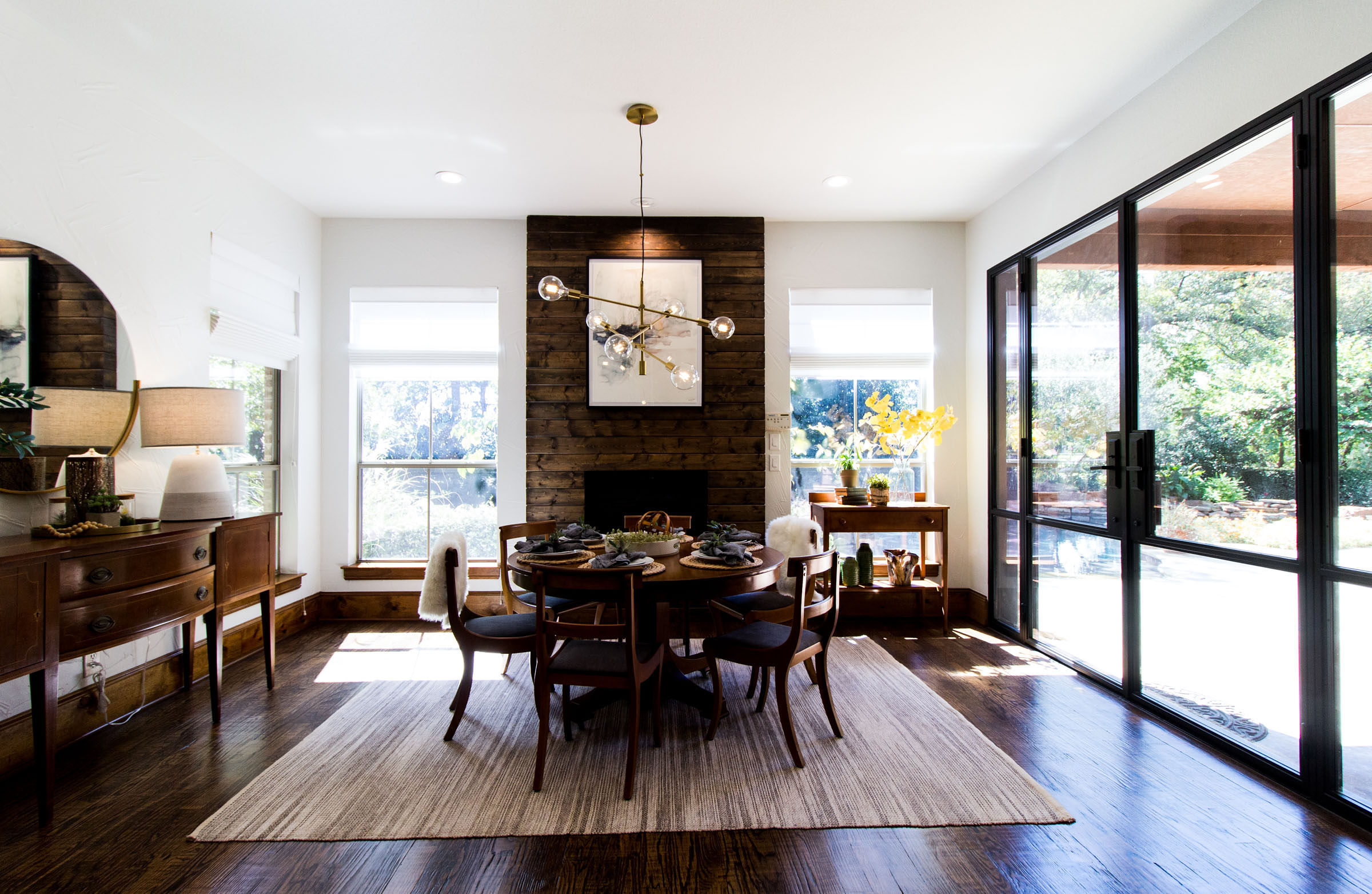 Cozy breakfast nook area with wood fireplace, iron framed patio doors, grey area rug, staged table, exposed bulb lighting