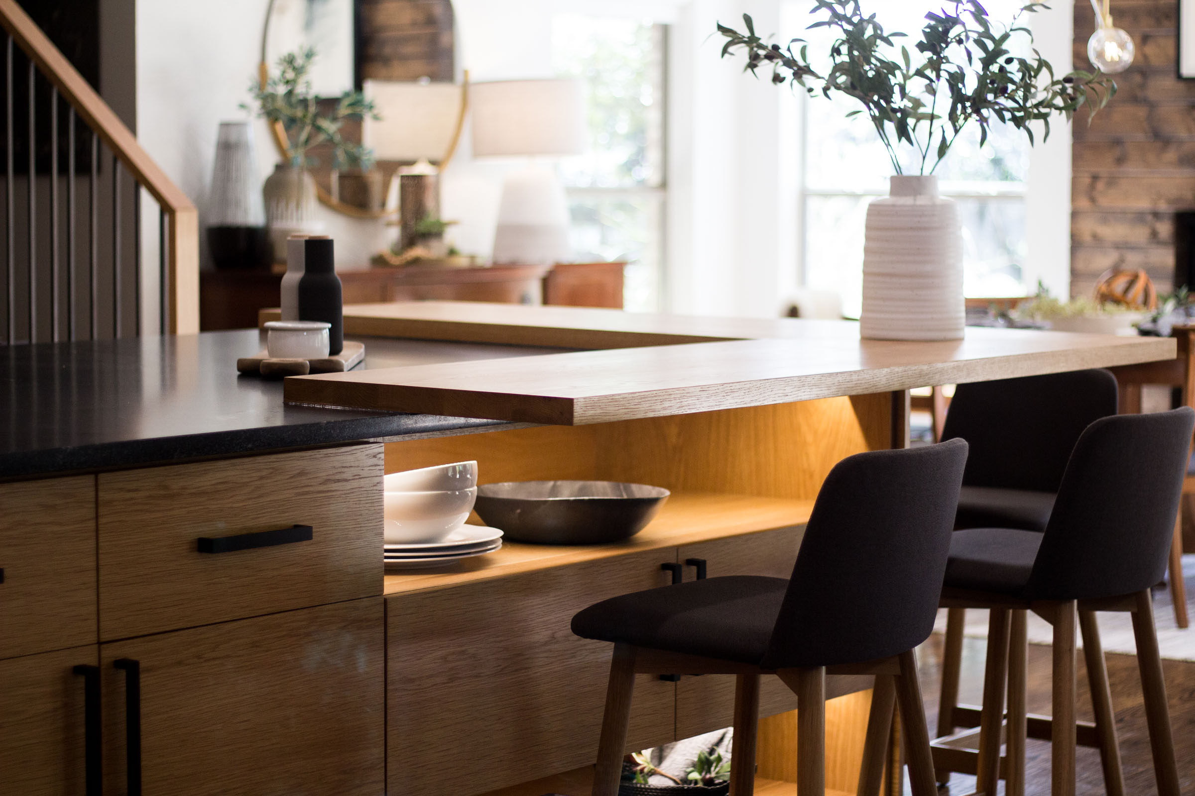 Cabinet under lighting with open cabinet space for kitchen dishes. Blonde wood cabinets, black cloth bar stools, plants, open floor plan.