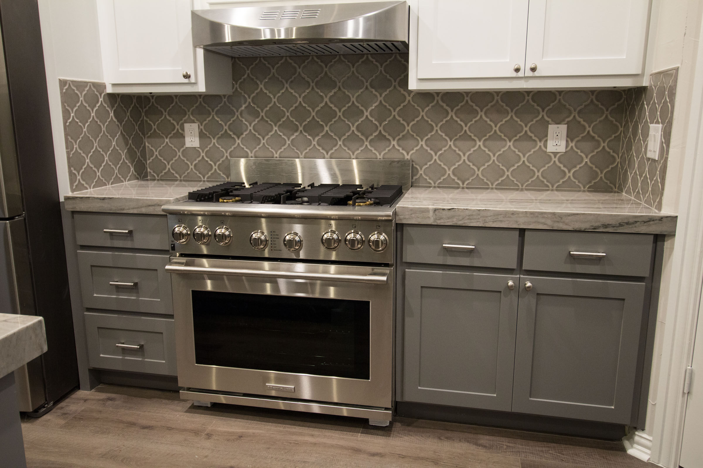 Contemporary kitchen remodel with industrial stainless steel gas cooking range, arabesque tile, grey shaker cabinets, white uppers, grey granite
