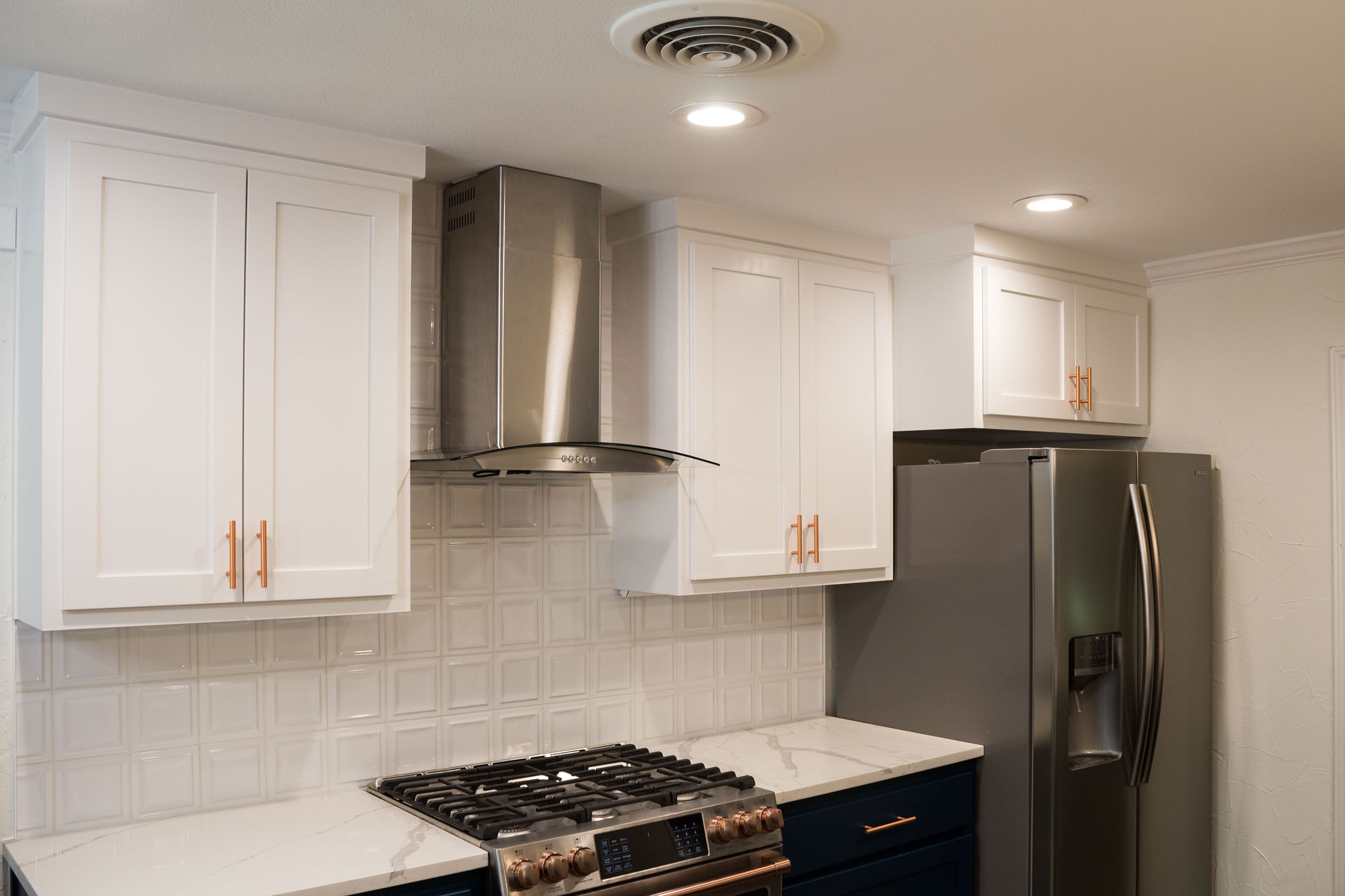 Stainless steel vent hood, copper hardware, white upper cabinets, navy lower cabinets
