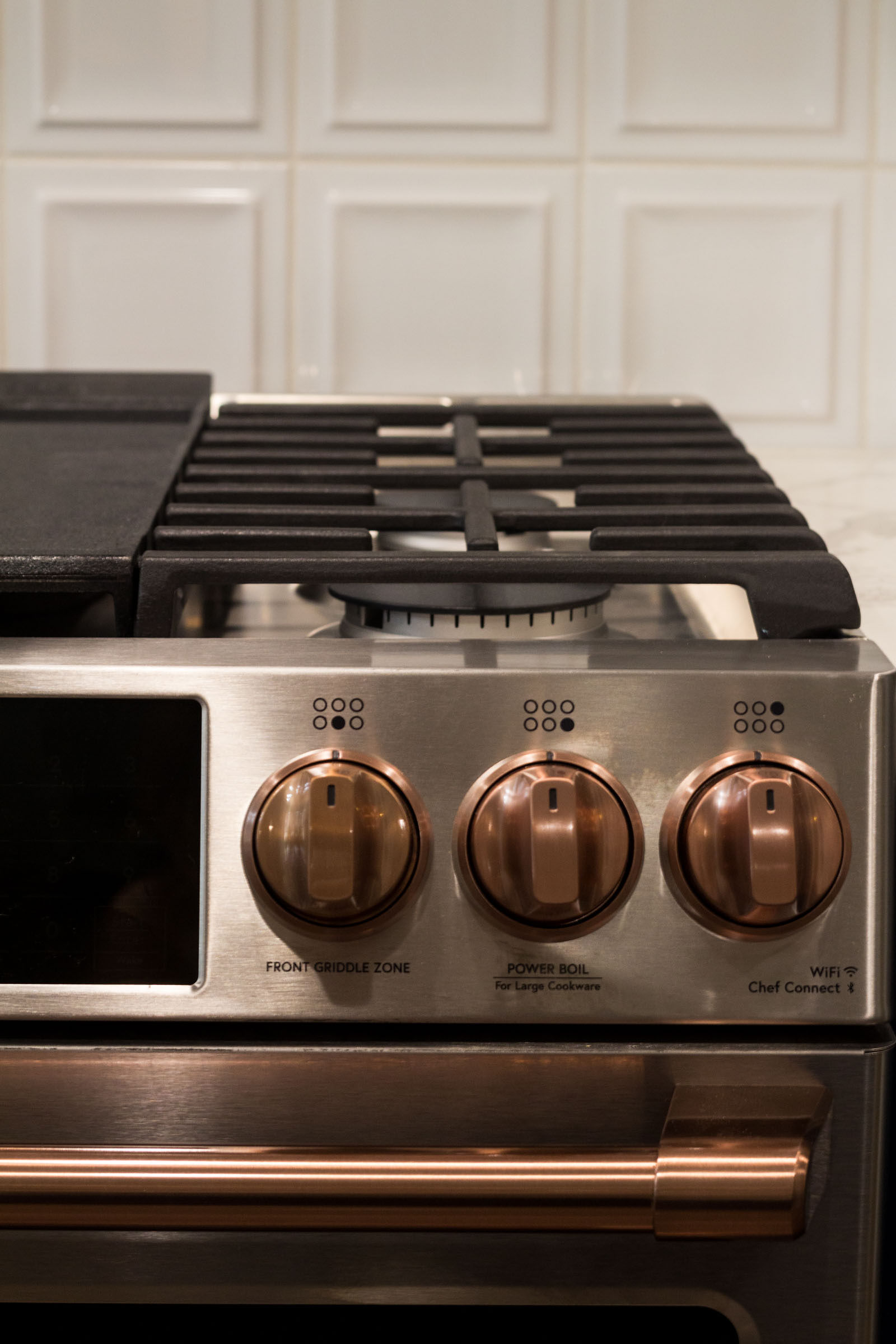 Close up of stainless steel gas cooking range with copper accents and white back splash