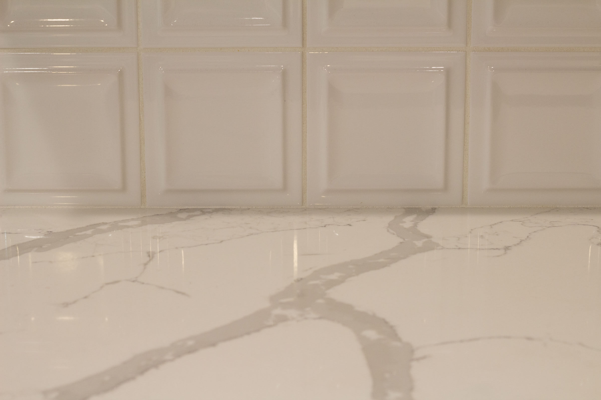 Close up photo of white countertops and square backsplash tiles